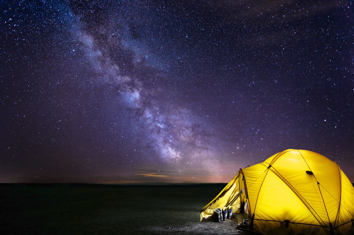 An illuminated yellow tent sits among the milky way galaxy