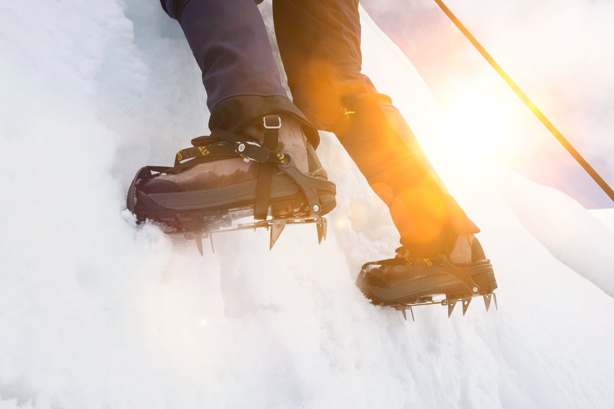 A hiker wearing boots and crampons ascends an icy wall