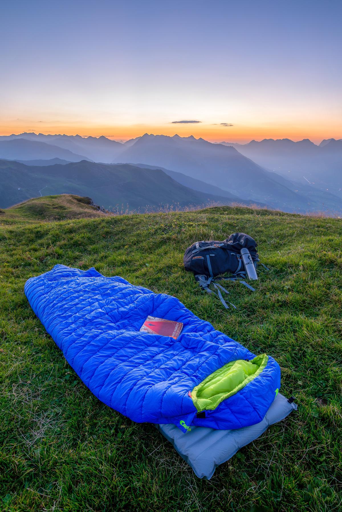 Image of a neatly folded sleeping bag with a serene camping scene in the background